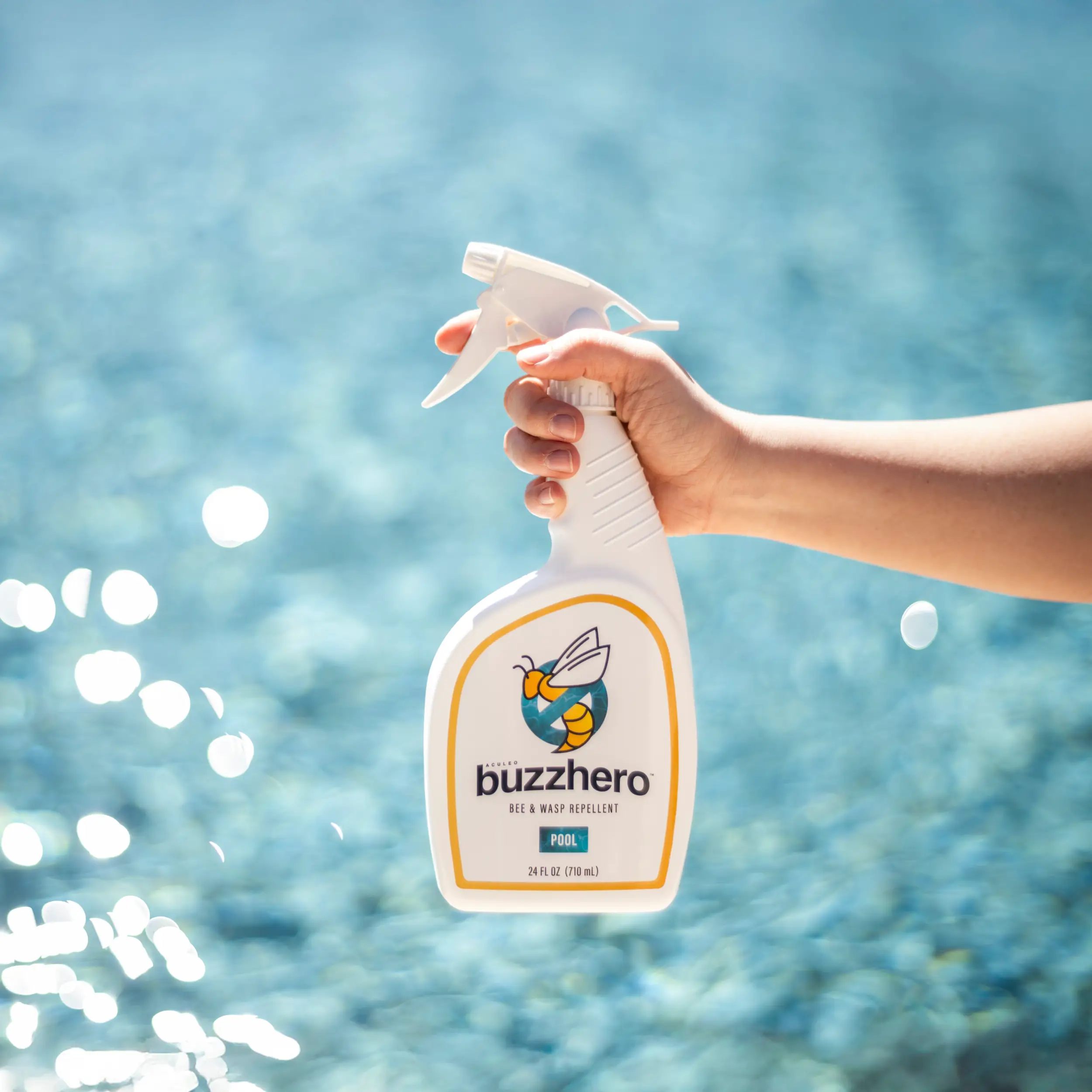 Hand holding a BuzzHero bee and wasp repellent spray bottle near a swimming pool.