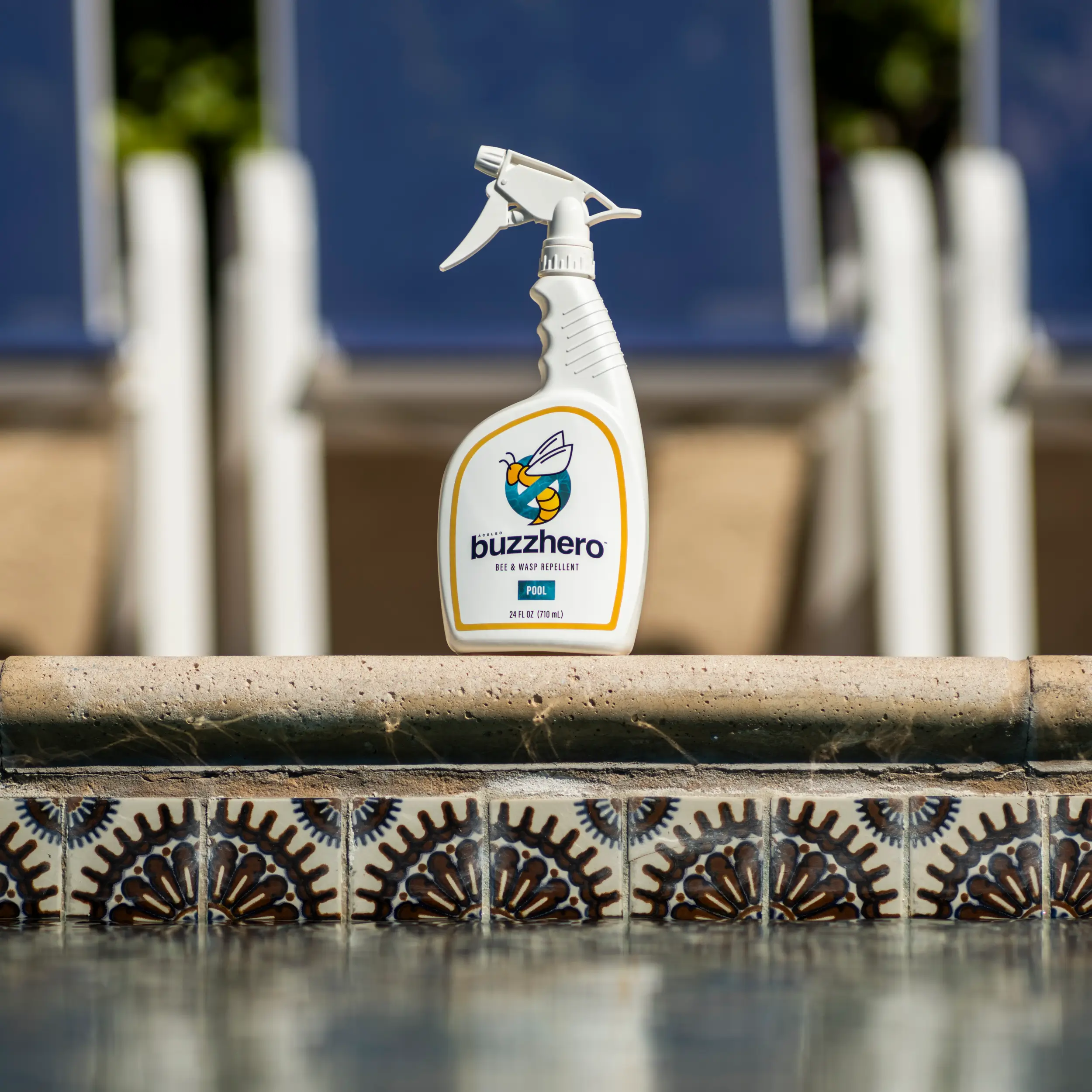 BuzzHero bee and wasp repellent spray bottle placed beside a swimming pool with patterned tile edge.