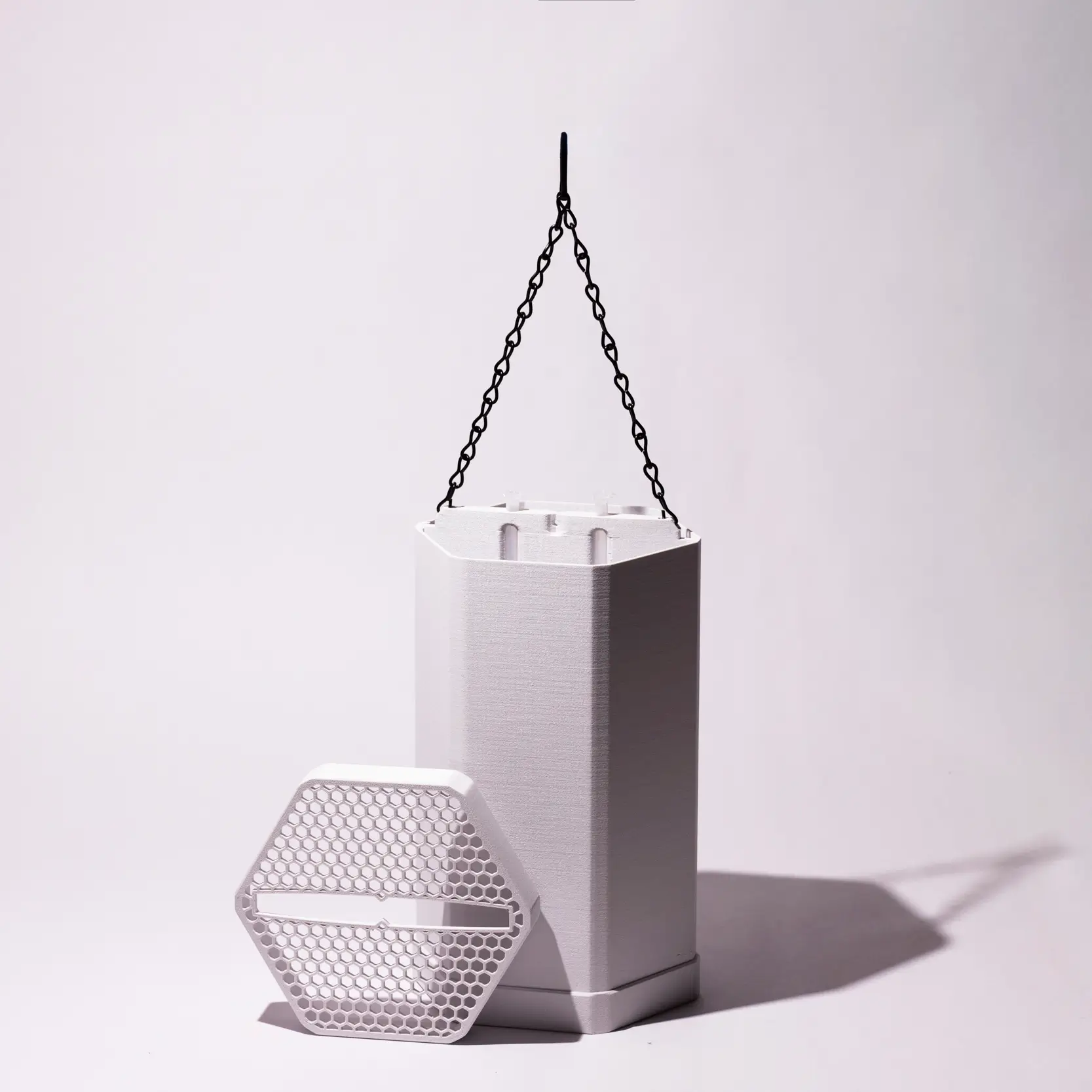 White hexagonal ScoutStop device with a honeycomb-patterned cover and hanging chain displayed on a light gray background.