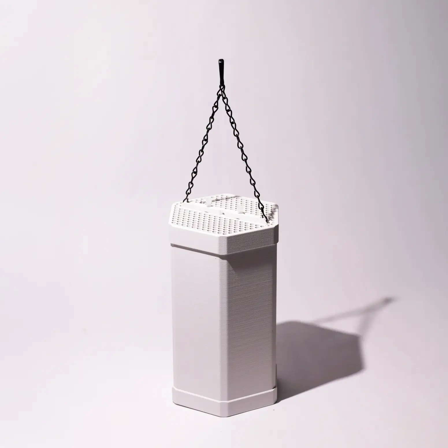 ScoutStop hanging mosquito trap in a hexagonal white casing with a perforated top and a black chain for outdoor suspension in a gray backgraound.